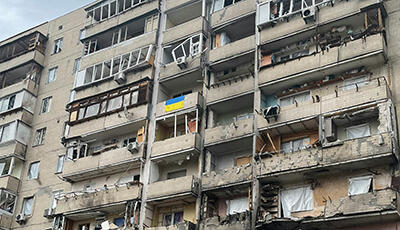 Zerstörte Fassade eines Hochhauses in Kiew, Ukraine. Über einer Balkonbrüstung hängt eine ukrainische Flagge.